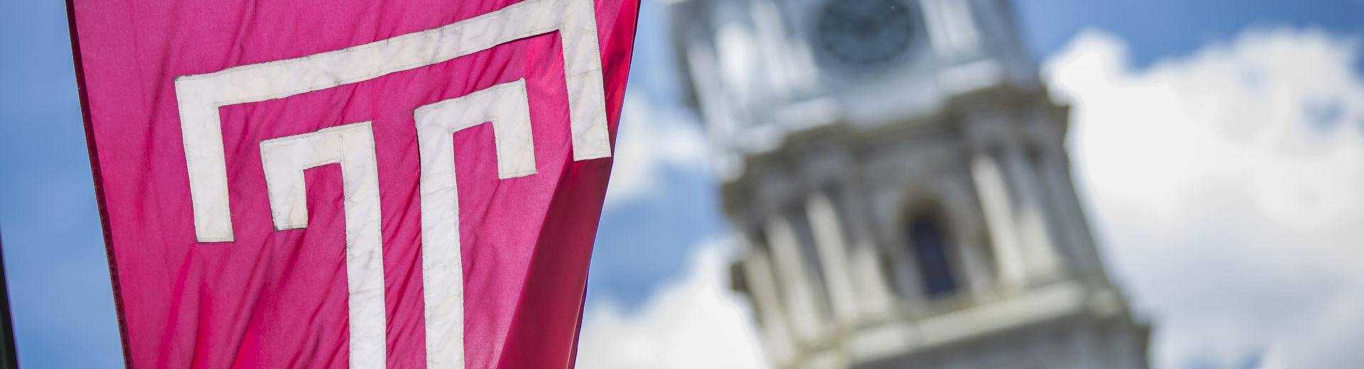 在一个阳光明媚的日子里，费城市政厅前飘扬着樱桃红色的Temple T旗.