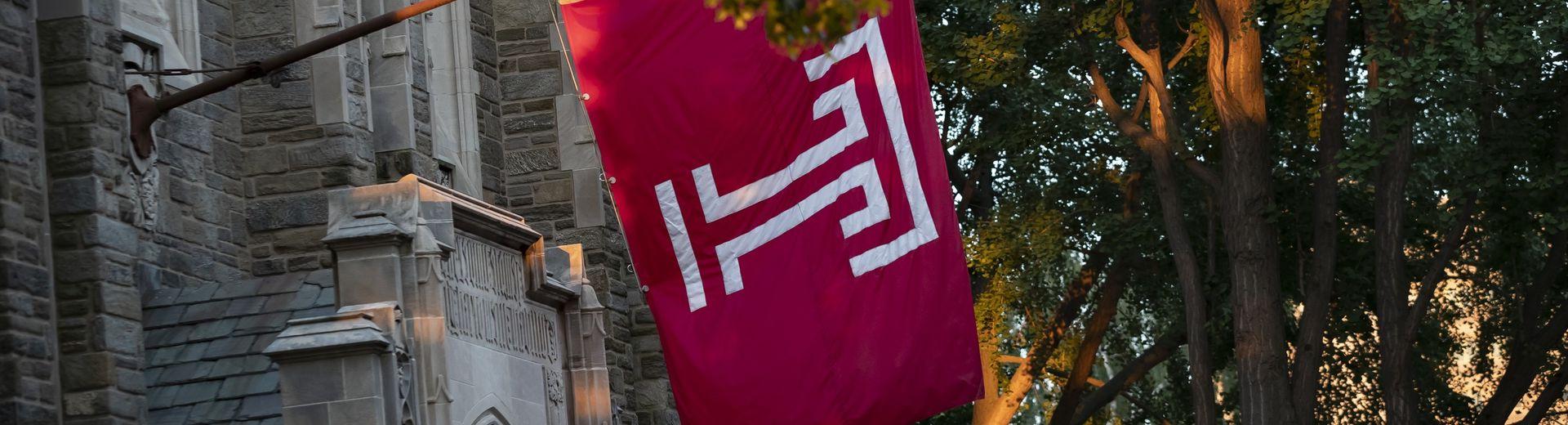 The cherry red Temple T flag hanging outside of Sullivan Hall on Main Campus